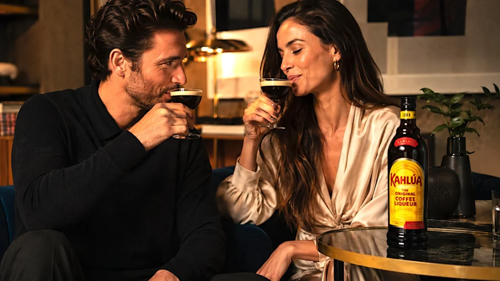 Pareja disfrutando un vaso de licor de café Kahlúa junto a una botella de la marca sobre una mesa en un ambiente elegante.